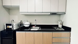 Eine kleine Küche mit weißen Schränken, einer schwarzen Arbeitsplatte, einer Mikrowelle, einem Spülbecken und einem kleinen Kühlschrank.