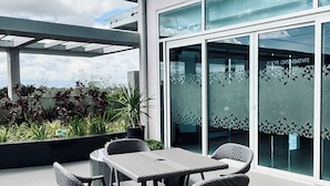 Eine Terrasse im Freien mit Tisch und Stühlen, eine Glastür mit geometrischen Mustern und Blick auf Himmel und Wolken.
