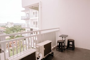 A balcony with a white railing, a small table, two stools, and a white air conditioning unit.
