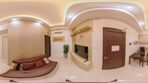 Un salon moderne avec un canapé aux lignes courbes, un téléviseur à écran plat, une porte en bois et un coin repas comprenant une table et des chaises.
