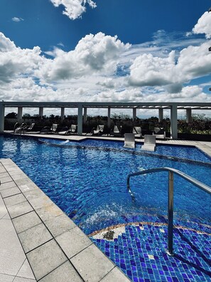 A swimming pool with clear blue water, surrounded by lounge chairs and a covered area.
