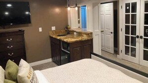 Un dormitorio con cama, televisor, baño con lavamanos y armario con puertas de cristal.