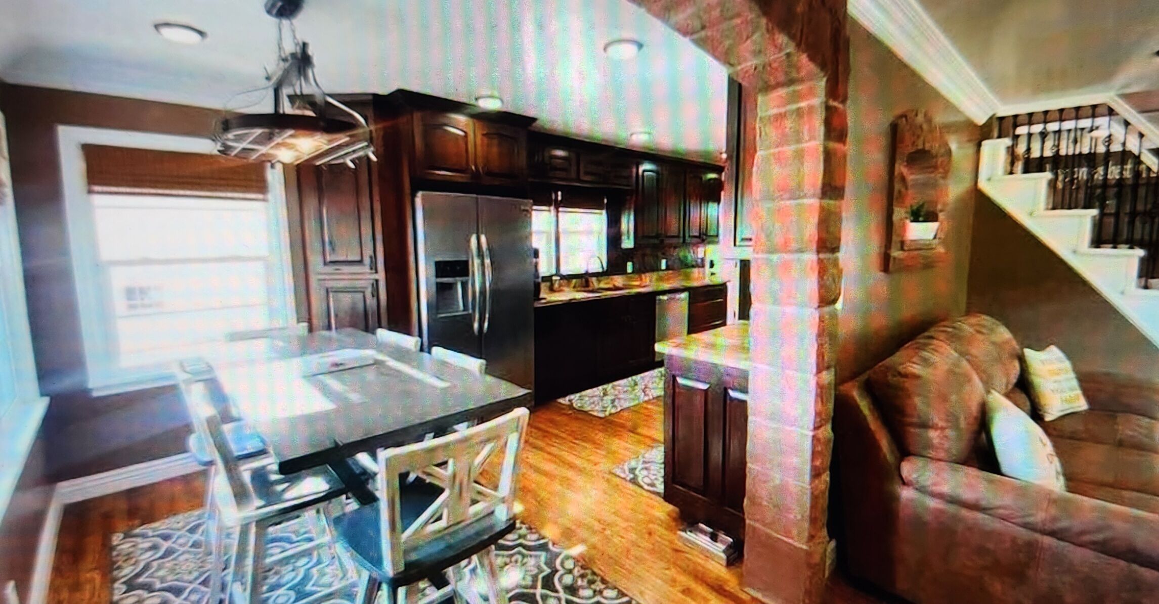 A modern kitchen with dark wood cabinets, a stainless steel refrigerator, and a dining area with a glass table and chairs.