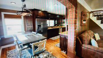 A modern kitchen with dark wood cabinets, a stainless steel refrigerator, and a dining area with a glass table and chairs.
