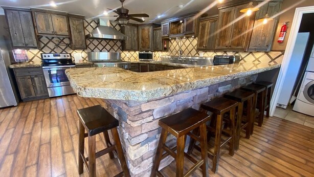 Una cocina con una isla grande, armarios de madera, una campana extractora de acero inoxidable y un ventilador de techo.