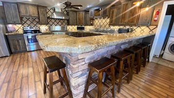 A kitchen with a large island, wooden cabinets, a stainless steel range hood, and a ceiling fan.