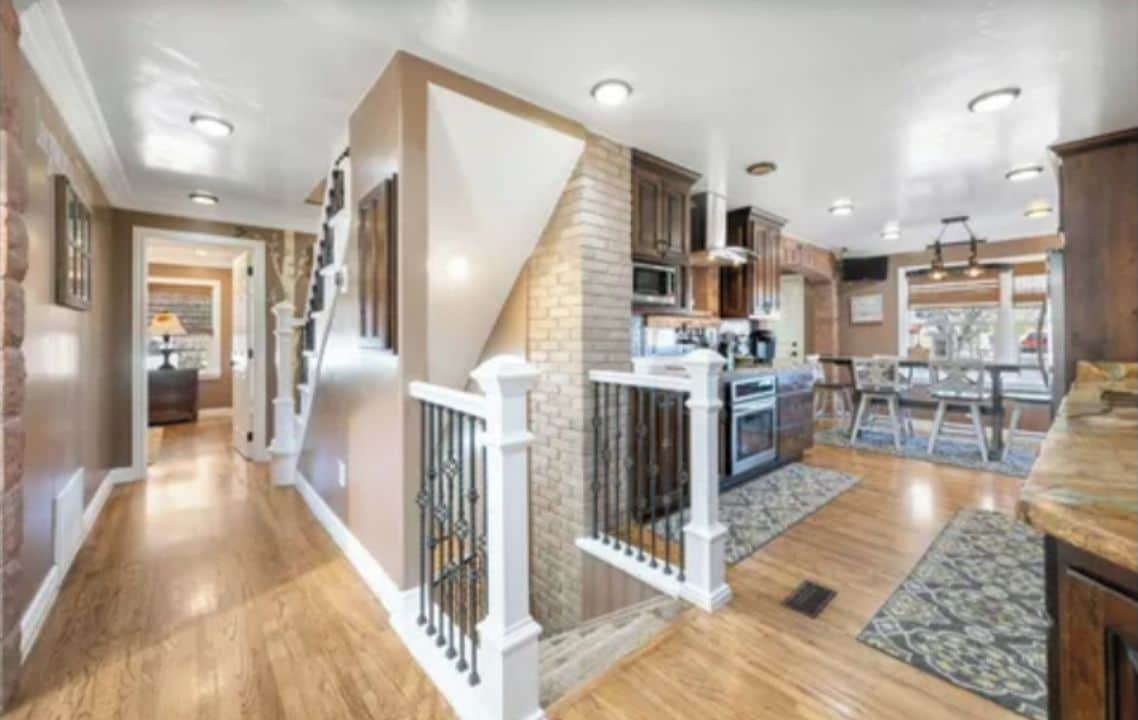 A spacious kitchen with a central island, wooden flooring, and a staircase leading to an upper level.