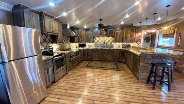 A modern kitchen with stainless steel appliances, a stone accent wall, and a wooden floor.