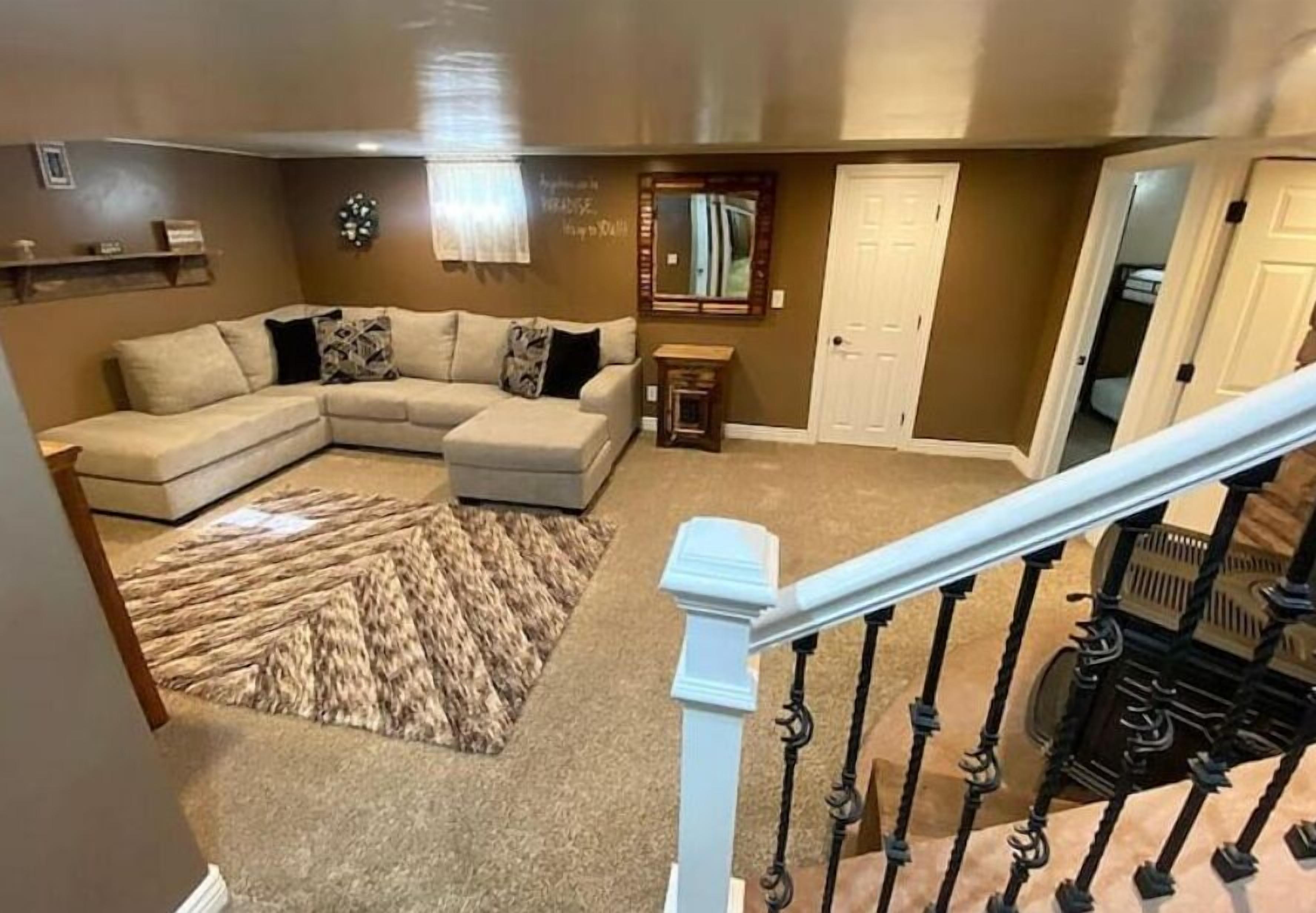 Un salon comprenant un canapé d’angle, un tapis à motifs, une petite table d’appoint et un escalier avec des rampes noires.