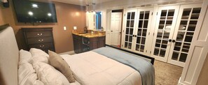 Ein Schlafzimmer mit Bett, Kommode, Fernseher, Waschtisch und einem Kleiderschrank mit Glastüren.