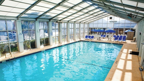 Una piscina interior con paredes de vidrio transparente, sillas y sombrillas azules.