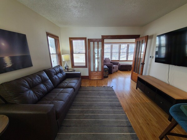 A living room with a leather sofa, a TV, and a wooden floor.