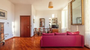 Un salon spacieux doté d’un plancher en bois, d’un canapé rose, d’un coin repas avec des chaises, d’une bibliothèque et d’un grand miroir.