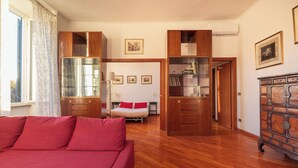 Une pièce spacieuse avec un plancher en bois, un canapé rouge, un lit avec des oreillers rouges et une armoire en bois dotée de portes en verre.