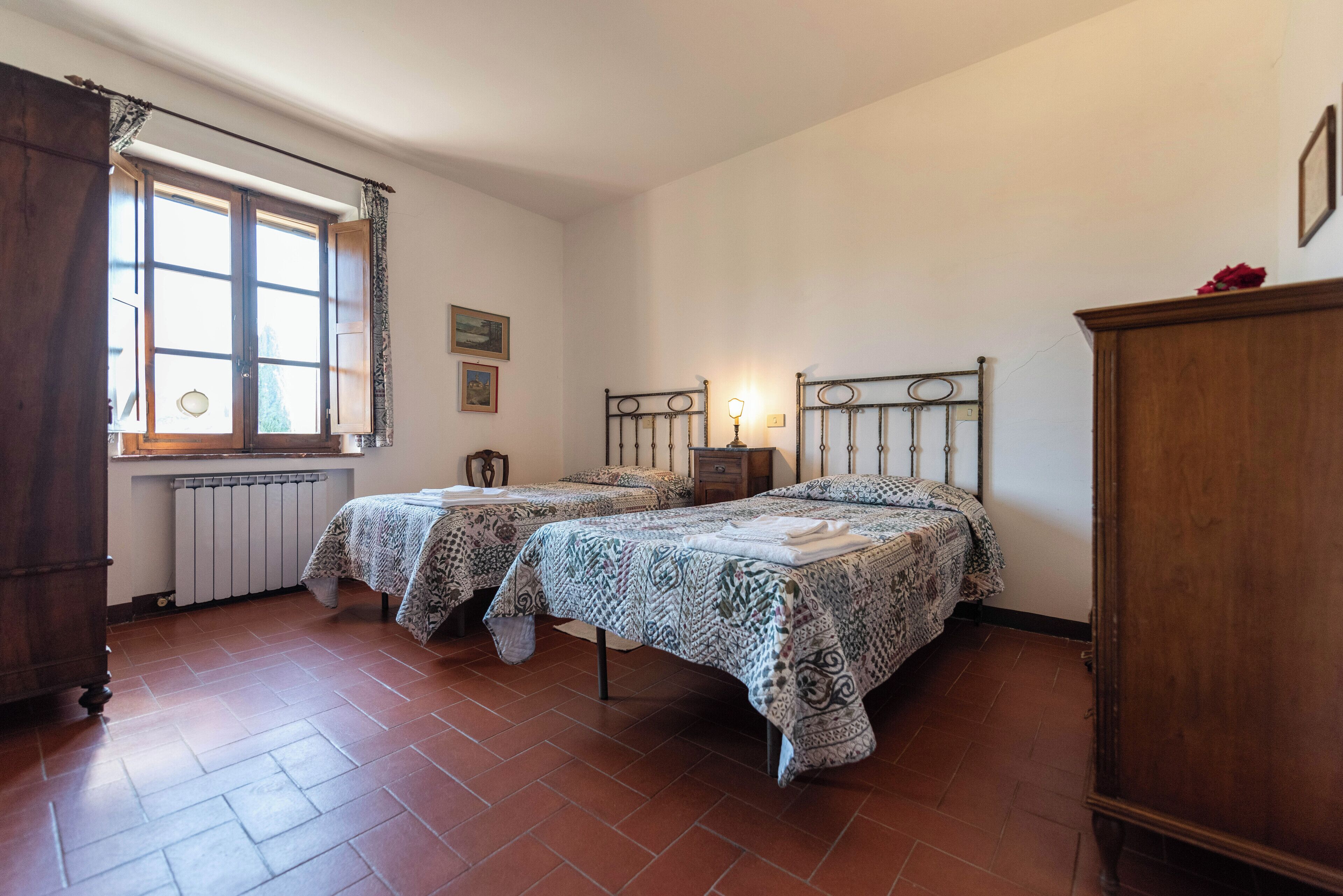 Ein Schlafzimmer mit zwei Betten, einem Heizkörper, einem Fenster mit Vorhängen und einem Holzschrank.