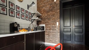 Une cuisine moderne avec des meubles en bois foncé, un plan de travail blanc et un mur en briques. On peut voir des certificats encadrés accrochés au mur, une machine à café et, au premier plan, une chaise rouge.