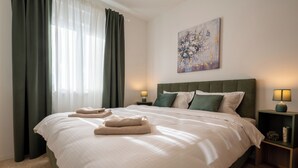 Una cama bien hecha con dos toallas, un cabecero verde y un cuadro en la pared.