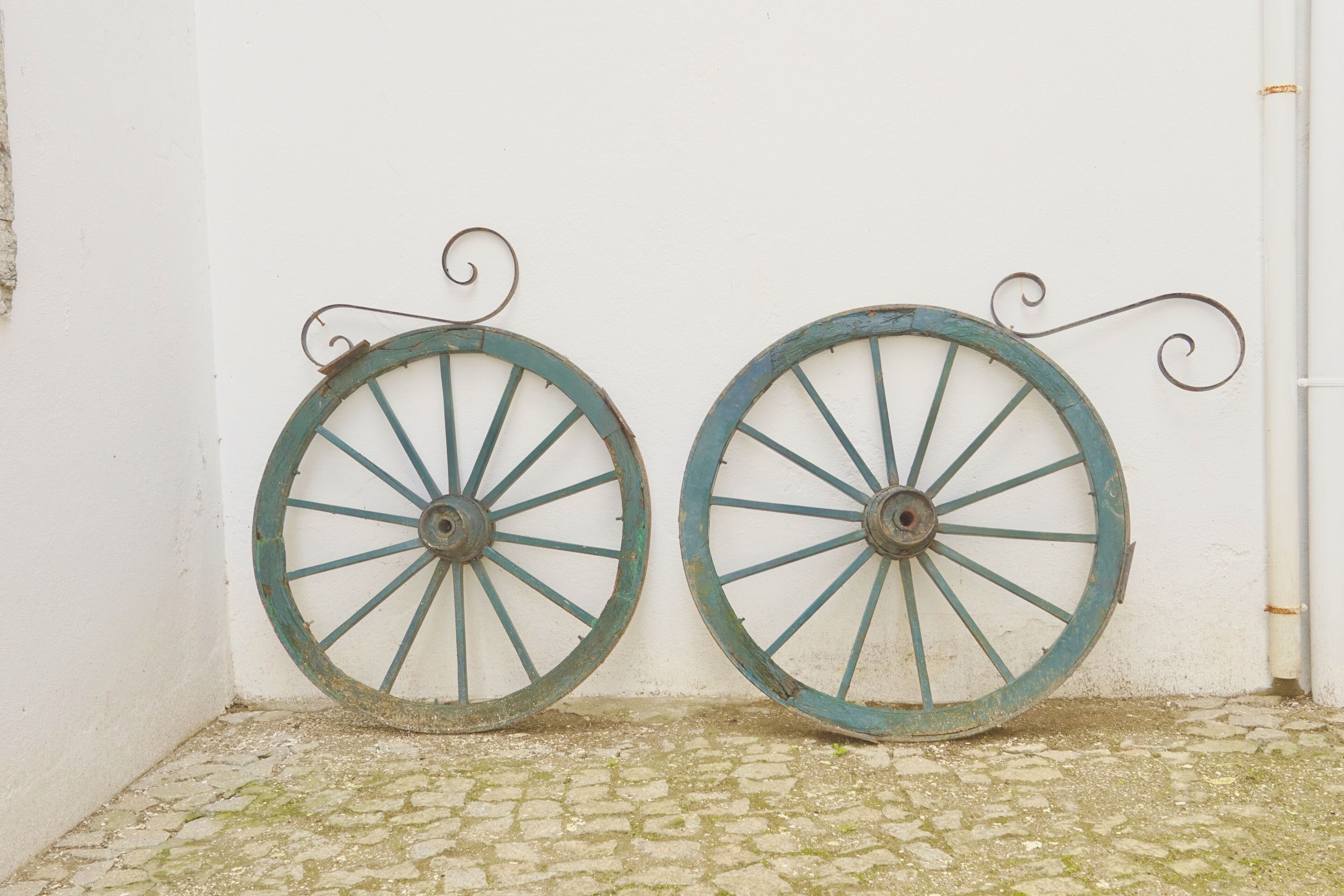 Two rustic, weathered wheels mounted on a white wall, with a cobblestone floor below.