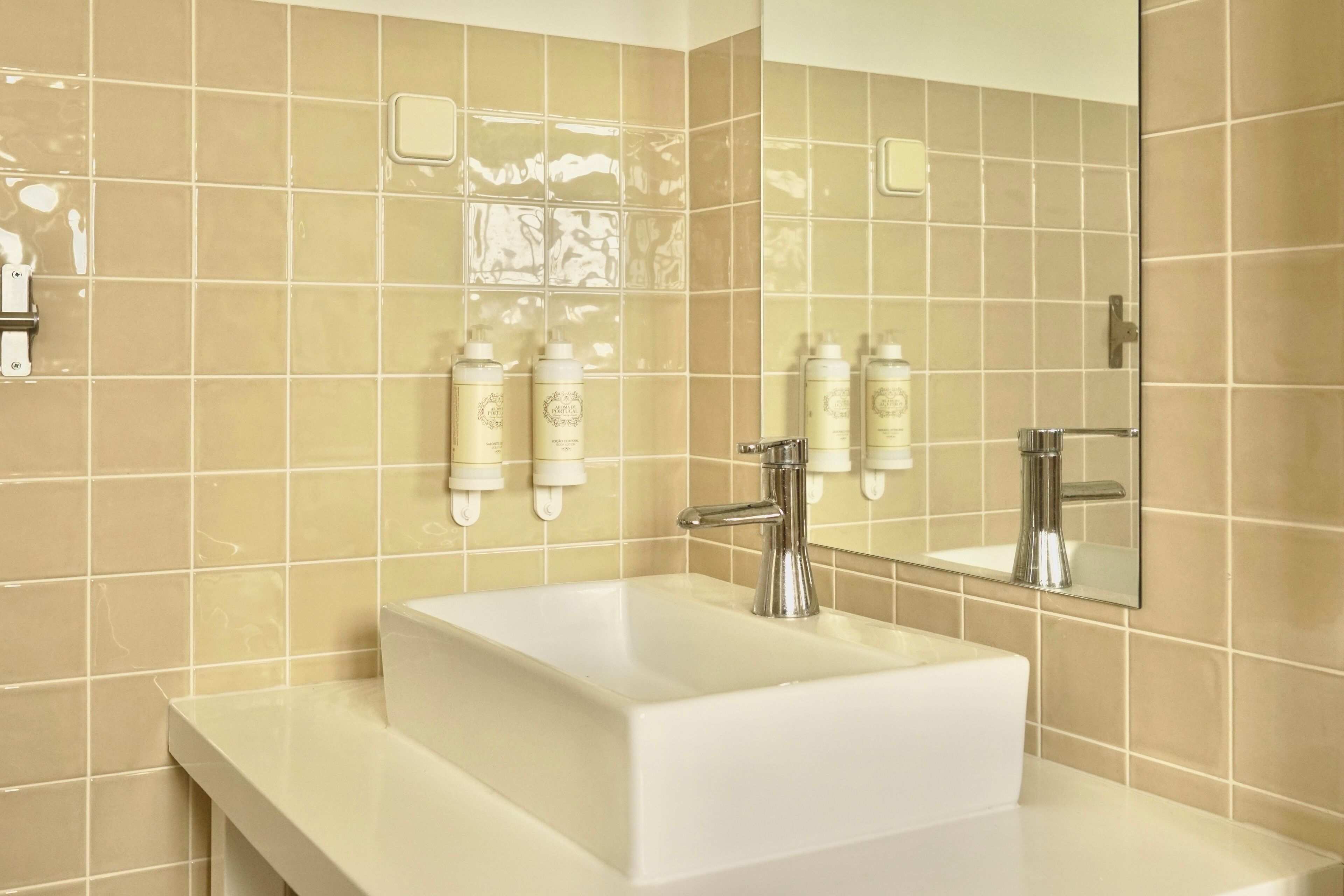 A bathroom with a white sink, chrome faucet, and beige tiled walls.