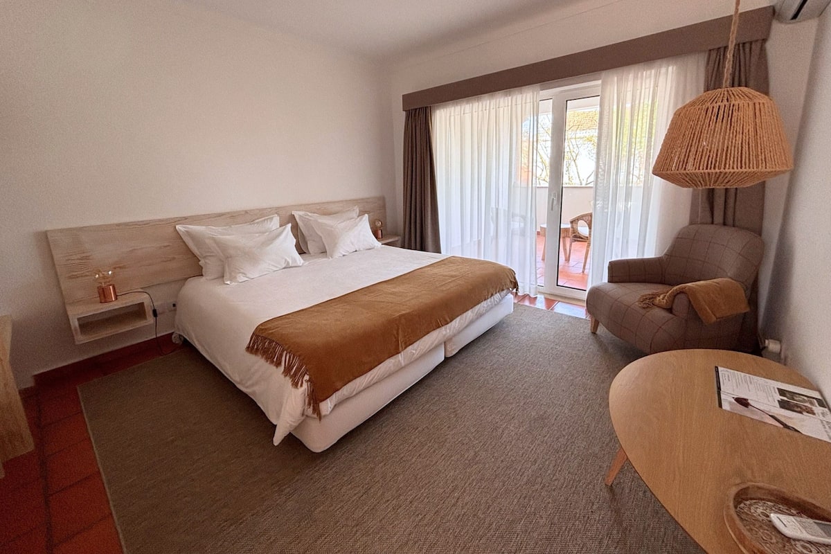A hotel room with a bed, a chair, a desk, and a window with curtains.