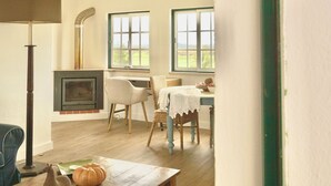 Una habitación acogedora con chimenea, una mesa de comedor, sillas y ventanas grandes con vistas al exterior.
