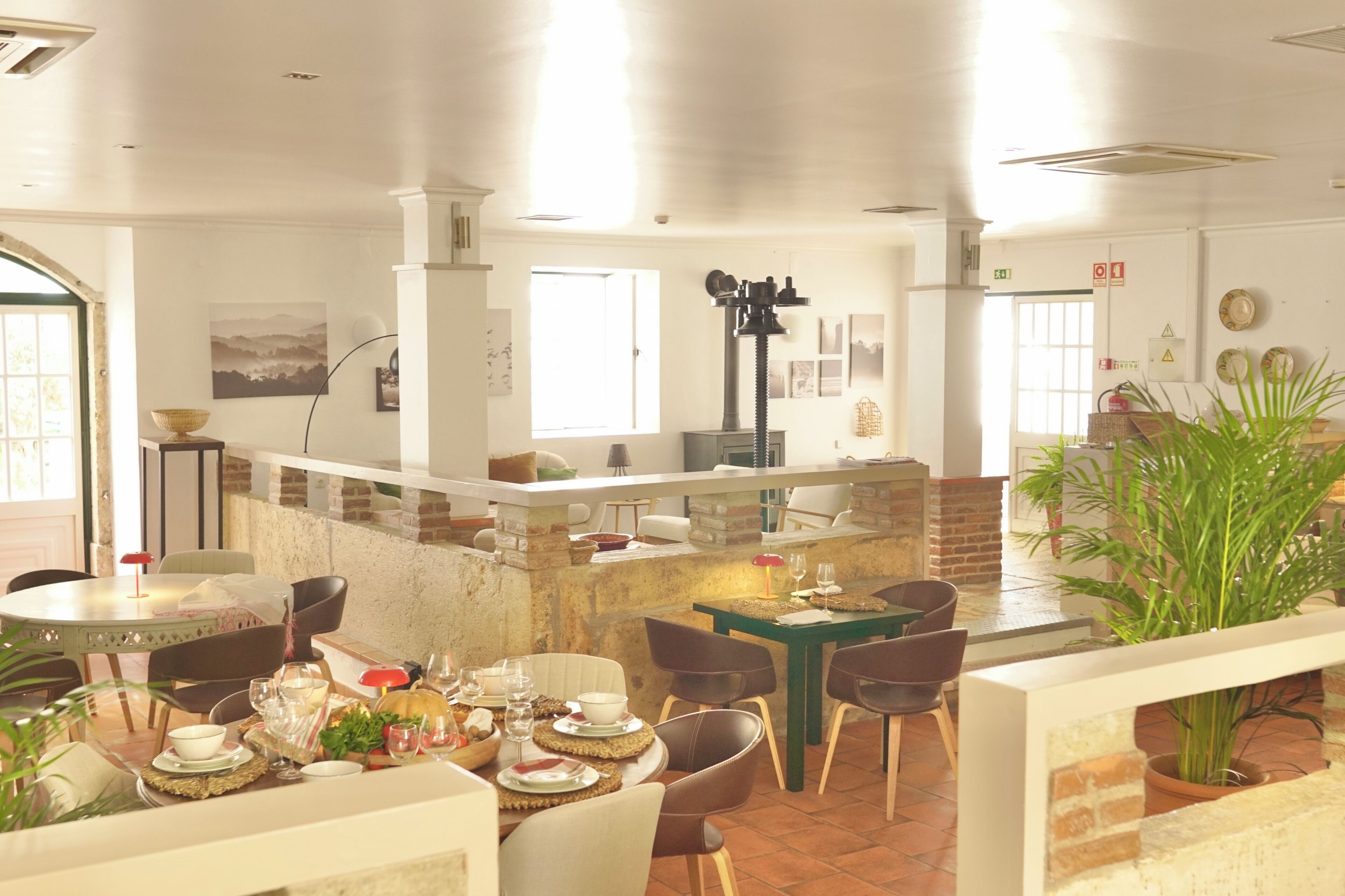 A dining area with a brick wall, a central island with a black lamp, and a view of the kitchen in the background.