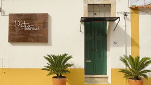 Un edificio con un letrero que dice "Patio das Ribeiras" y una puerta verde. Hay dos plantas en macetas en la entrada.
