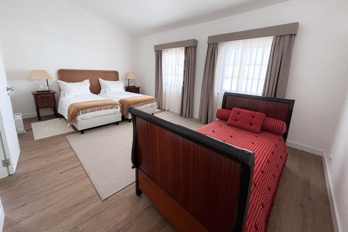 A hotel room with two beds, a wooden headboard, a red bedspread, and a small bedside table with a lamp.