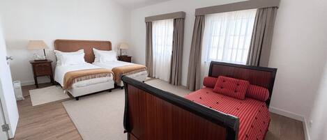 A hotel room with two beds, a wooden headboard, a red bedspread, and a small bedside table with a lamp.