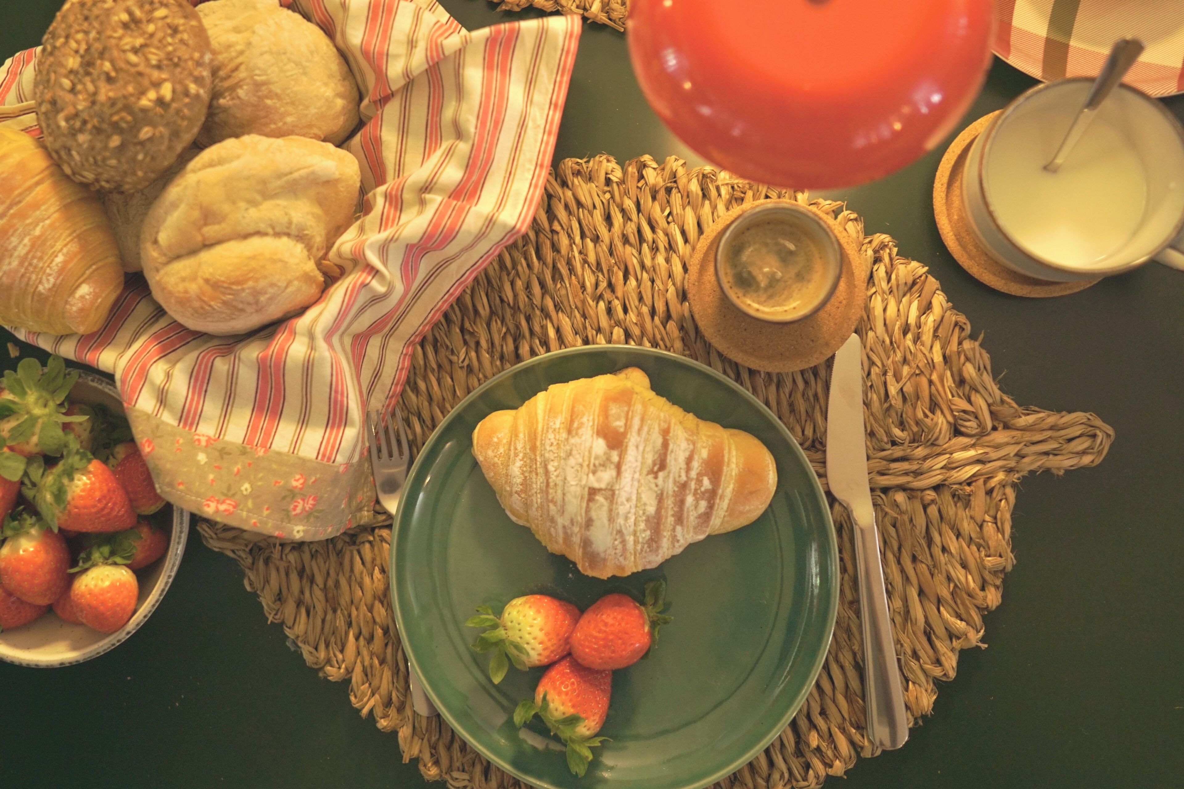 A table with a croissant, strawberries, a bowl of strawberries, a basket of bread, a glass of milk, and a red balloon.