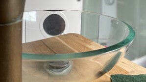 Un baño con un lavabo de cristal, un grifo de bronce y un box de ducha de vidrio.