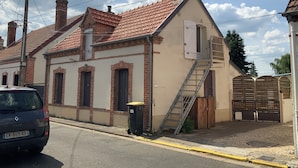 Un edificio de dos pisos con techo de tejas rojas, una chimenea de ladrillo y una puerta blanca.