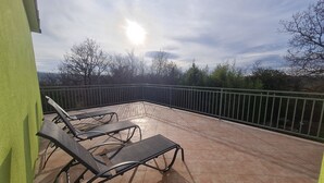 En solbeskinnet udendørs terrasse med liggestole og flisegulv.