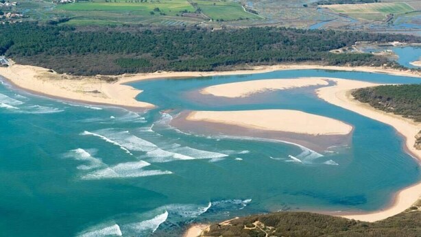 Vista aérea de una zona costera con playas de arena, aguas azules cristalinas y terrenos boscosos circundantes.