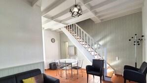 Un amplio salón con un sofá de cuero negro, una mesa de comedor con sillas, una escalera y una lámpara moderna.