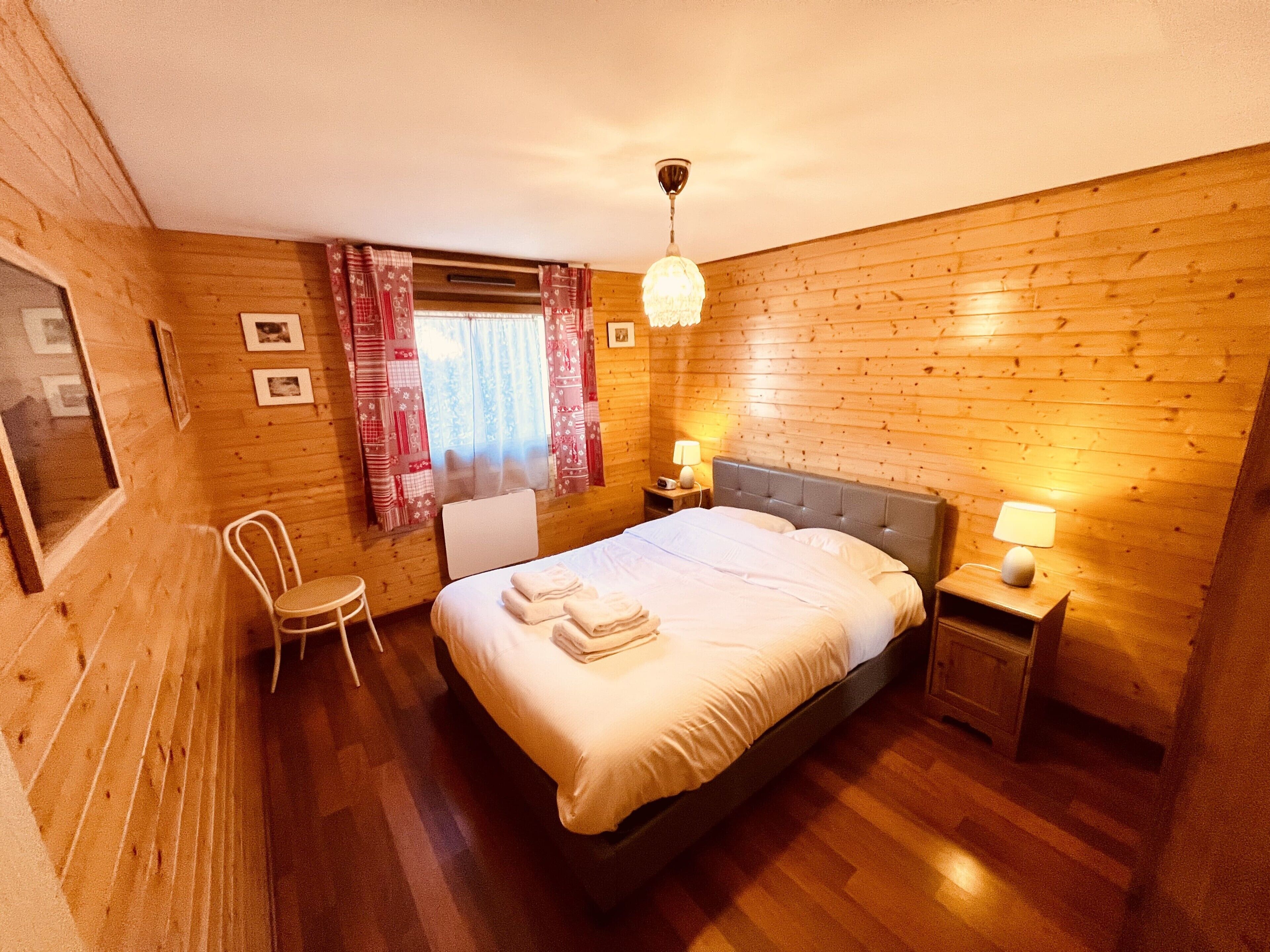 Un cuarto acogedor de madera con una cama, una silla y dos mesitas de noche con lámparas.