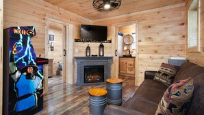 Ein gemütliches Blockhaus-Interieur mit Kamin, Fernseher und einem Midway-Arcade-Spiel.