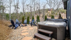 Eine Terrasse im Freien mit Adirondack-Stühlen, einem Whirlpool und einer Feuerstelle.