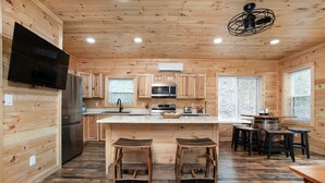 A wooden cabin-style kitchen with a central island, bar stools, and a dining table.