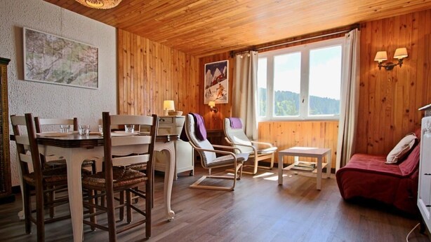 Ein gemütliches Zimmer mit Holzbalkendecke, einem Esstisch mit Stühlen, einem Sofa, einem kleinen Tisch und einem Bett.