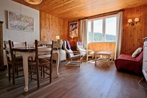 A cozy room with a wooden ceiling, a dining table with chairs, a sofa, a small table, and a bed.