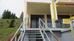 Ein Gebäude mit einer Treppe, die zu einer Tür führt, umgeben von einer Grünfläche und Bäumen.