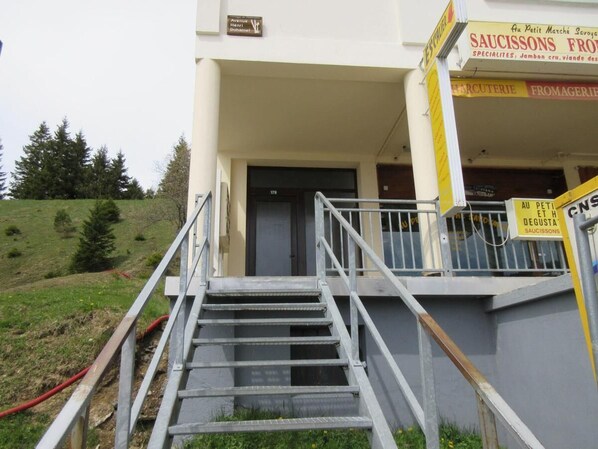 A building with a staircase leading to a door, surrounded by a grassy area and trees.