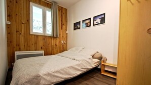 Ein Schlafzimmer mit einer Holzwand, einem Bett mit gemustertem Überwurf, einem Nachttisch, einer kleinen Ablagefläche und einem Kleiderschrank.