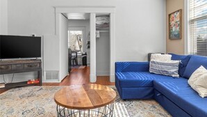 Una sala de estar con un sofá azul, una mesa de centro redonda de madera y un televisor de pantalla plana sobre un mueble de madera oscura.
