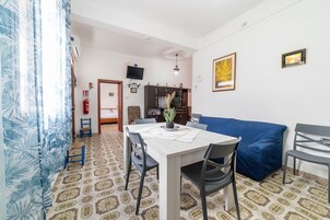 Un comedor con una mesa, sillas y un sofá azul. Hay un televisor montado en la pared y un extintor.