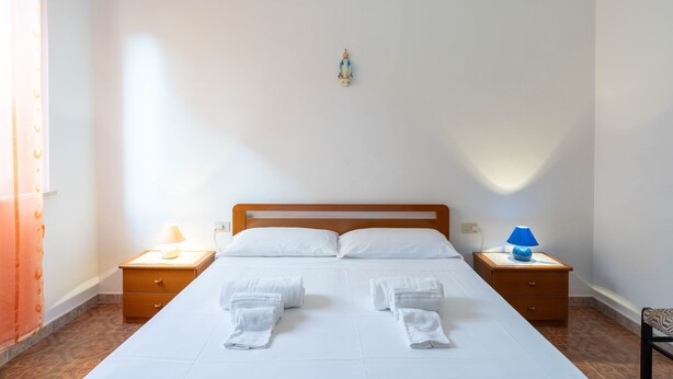 Un lit bien fait, avec du linge de lit et des serviettes blanches, deux tables de chevet avec des lampes, une tête de lit en bois et un petit objet décoratif accroché au mur.
