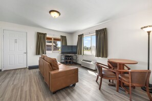 A furnished room with a sofa, a television, a dining table with chairs, a standing lamp, and a window with curtains. - White River Inn (Meeker)