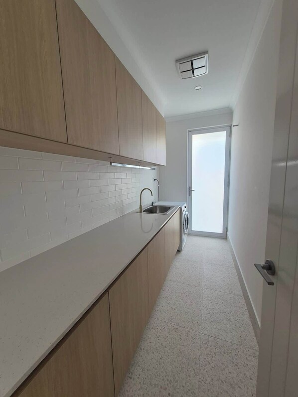 Une cuisine moderne avec des meubles en bois, un plan de travail blanc, un évier encastré et un lave-linge.