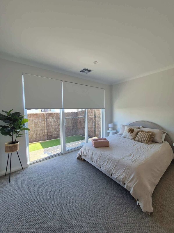 A bedroom with a bed, a potted plant, a sliding glass door, and a view of a fenced yard.